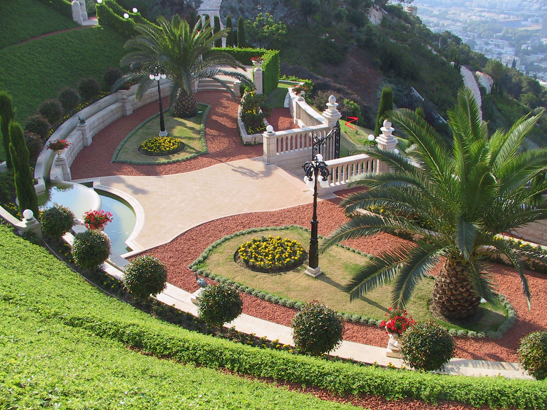 A manicured upper terrace of the Baha'i Gardens in Haifa: date palms, clipped topiary, a stone balustrade and a fountain in warm sun